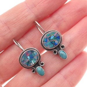 May include: Silver-tone earrings with oval-shaped, mosaic-style opal stones in shades of blue, green, and purple. Each earring has a small, turquoise-colored stone at the bottom. The earrings are displayed against a light background.