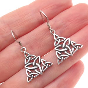 May include: A pair of silver-toned Celtic knotwork earrings. Each earring features a triangular design with interwoven knot patterns, suspended from a simple hook. The earrings are displayed against a light background.