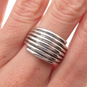 May include: A wide silver ring featuring a series of parallel, raised horizontal bands that wrap around the finger. The metal has a polished, reflective finish with deep grooves between each of the rounded, stacked wire-like silver segments.