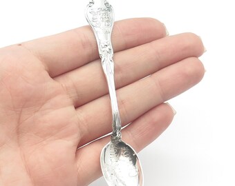 May include: A silver souvenir spoon with an ornate handle and a rounded bowl. The bowl features an engraved design of a building with the text "The Breakers" on the front.