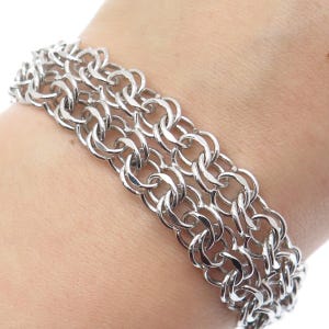 May include: A silver chain bracelet with a multiple-row design. The bracelet is made of interlocking oval links.