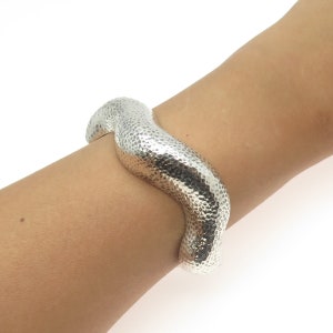 May include: A silver hammered bangle bracelet with a wavy, organic shape.