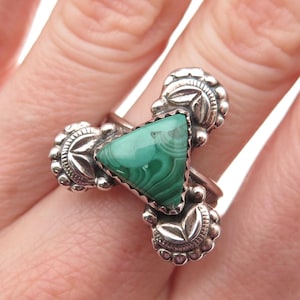 May include: A silver ring featuring a triangular, vibrant green malachite stone. The ring has a decorative design with floral and beaded accents. The malachite displays a unique swirling pattern. The ring is a piece of jewelry.