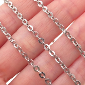 May include: Close-up of three silver-colored chain necklaces. The chains are made of small, flat, circular links connected together. The chains are displayed against a light pink background.