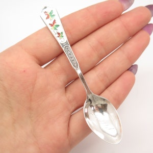 May include: Silver souvenir spoon with a red, green, and white enamel maple leaf design. The handle is engraved with the word "CANADA".