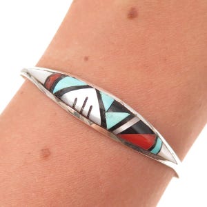 May include: A silver cuff bracelet featuring a central marquise-shaped inlay design. The inlay consists of geometric segments of turquoise, red coral, black onyx, and white shell, arranged in a pattern with thin silver dividers between stones.