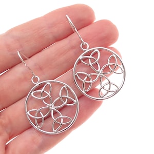 May include: A pair of silver-toned dangle earrings featuring a circular frame. Inside each circle is an intricate, interconnected triquetra knot design. The earrings are attached to simple silver-toned ear wires for hanging, creating a balanced look.