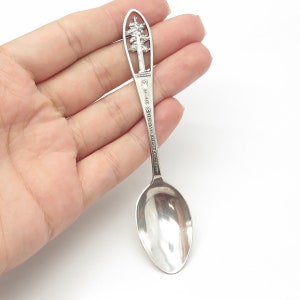 May include: Silver souvenir spoon with a tree design on the handle. The handle is engraved with "Muir Woods National Monument".