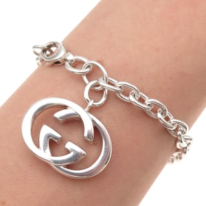 May include: A silver chain link bracelet featuring a large, circular, open-work charm with the interlocking G logo. The bracelet is constructed from polished silver-toned metal links and includes a secure lobster claw clasp closure mechanism.