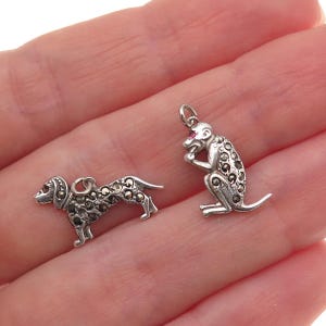 May include: Two small silver charms: a dog and a monkey. The dog charm is a dachshund-like breed, and the monkey is sitting with its hand to its mouth. Both charms are detailed with small, dark stones.