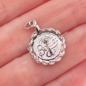 May include: A silver-toned pendant with a circular design featuring a palm tree and the word "Bahamas". The pendant has a rope-like border and a small loop for attaching to a chain or bracelet.