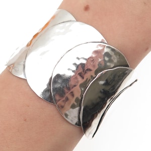 May include: A silver-toned bracelet with a hammered texture. The bracelet is composed of several large, overlapping, circular segments. The segments have a reflective, shiny surface. The bracelet is a piece of jewelry.