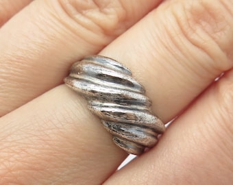 May include: A silver ring with a twisted, textured design. The ring is worn on a finger.