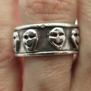 May include: Silver ring with a band of five smiling faces, each face is a separate design.
