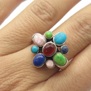 May include: A silver ring with a cluster of colorful gemstones. The stones are set in a silver band and are arranged in a random pattern. The stones are pink, red, blue, green, and turquoise.