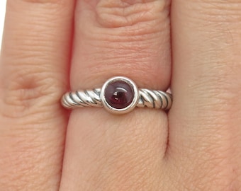 May include: A silver ring with a twisted band and a round, cabochon-cut, dark red gemstone.