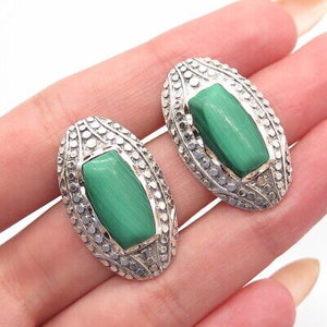 May include: A pair of sterling silver earrings with green malachite stones. The earrings are oval shaped and have a textured design.