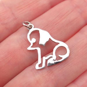 May include: A small, silver-colored pendant in the shape of a sitting dog. The dog's outline is clearly defined, with a loop at the top for attaching to a chain. The pendant is likely made of metal and has a polished finish.