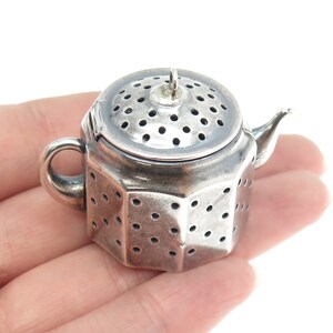 May include: Silver teapot-shaped tea infuser with a perforated lid and body. The infuser has a small handle and a spout.