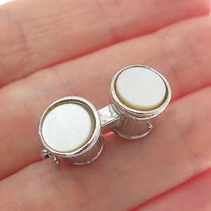 May include: Silver charm in the shape of a pair of bongo drums with white mother of pearl drumheads.