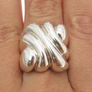 May include: A silver ring with a unique, abstract design. The ring is made of smooth, polished metal and has a rounded, organic shape.