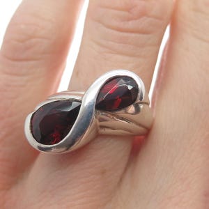 May include: A silver ring with two red gemstone accents. The ring is designed in a twisted, infinity-like shape.