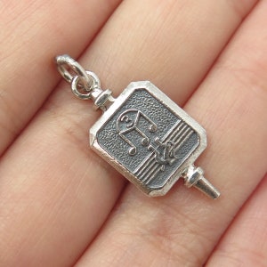 May include: Silver charm with a musical note design. The charm is shaped like a square with rounded corners and has a textured surface. The charm has a loop at the top for attaching to a bracelet or necklace.