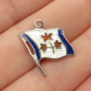May include: Silver charm with a white flag with three orange maple leaves and blue trim. The flag is on a silver pole.