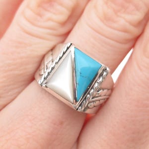 May include: A silver ring with a triangular design. One half of the triangle is white, and the other is turquoise. The ring has a braided design on the sides.
