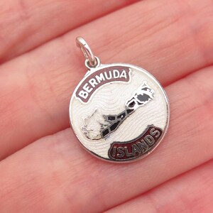 May include: A round silver charm with the words "BERMUDA" and "ISLANDS" in red lettering. The charm features a white background with a detailed map of Bermuda in black and white.