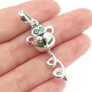 May include: Silver charm with a green enamel monkey head and a curled tail.