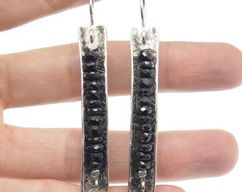 May include: A pair of silver earrings with black beads hanging from them. The earrings are rectangular in shape and have a textured surface.