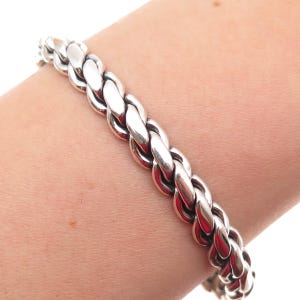 May include: A polished silver-tone bracelet featuring a thick, braided chain link design. The bracelet is composed of interlocking, rounded metal segments that create a continuous, rope-like texture around the wrist.