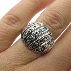 May include: A silver ring with a domed design featuring green and red gemstones set in a textured band.
