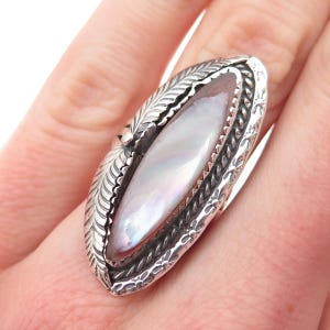 May include: A marquise-shaped ring featuring a central iridescent mother-of-pearl inlay. The silver setting is detailed with etched feather patterns on the sides, a twisted rope border, and small stamped flower motifs along the outer edges.