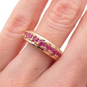 May include: A gold-toned ring featuring a row of vibrant, round, ruby gemstones. The ring's band has a smooth, polished finish, and the rubies are set closely together, creating a continuous line of color. The ring is a classic piece of jewelry.
