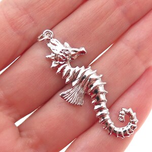 May include: A detailed silver seahorse pendant with a textured surface. The seahorse has a curled tail and a loop at the top for attaching to a chain. The pendant is a nautical-themed jewelry piece.