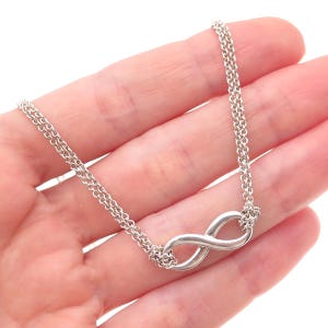 May include: A silver-toned bracelet featuring a central infinity symbol charm. The piece is constructed with a double-strand chain design, where two delicate metallic chains connect to each side of the polished infinity loop, creating a cohesive look.