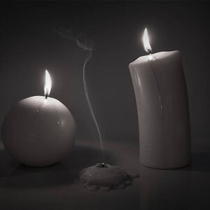 May include: Three white candles, two are lit and one is extinguished with a wisp of smoke rising from the wick.