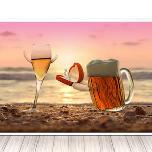 May include: A glass of white wine and a glass of beer on a beach at sunset. The beer glass is holding a red ring box with a diamond ring inside.