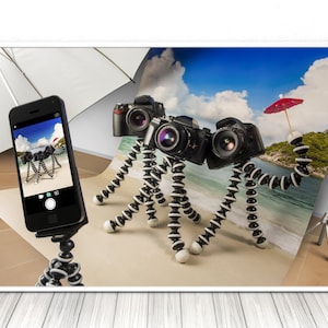 May include: Three cameras on flexible tripods are arranged to look like a creature with a red umbrella. The creature is taking a selfie with a smartphone on a tripod.