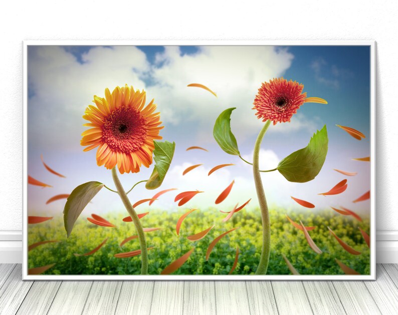 May include: A painting of two flowers, a yellow and orange sunflower and a red gerbera daisy, with green leaves and petals blowing in the wind against a blue sky with white clouds.