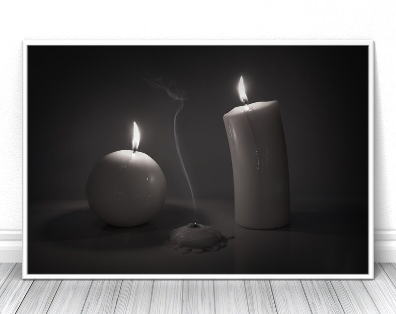 May include: Three white candles, two are lit and one is extinguished, with smoke rising from the extinguished candle. The candles are on a dark surface.