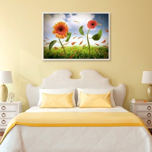 May include: A white bed with a yellow bedspread and two yellow pillows. A framed picture of two sunflowers with orange and red petals is hanging on the wall above the bed.