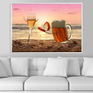 May include: A glass of white wine and a glass of beer on a sandy beach at sunset. The beer glass is holding a red ring box with a diamond ring inside.