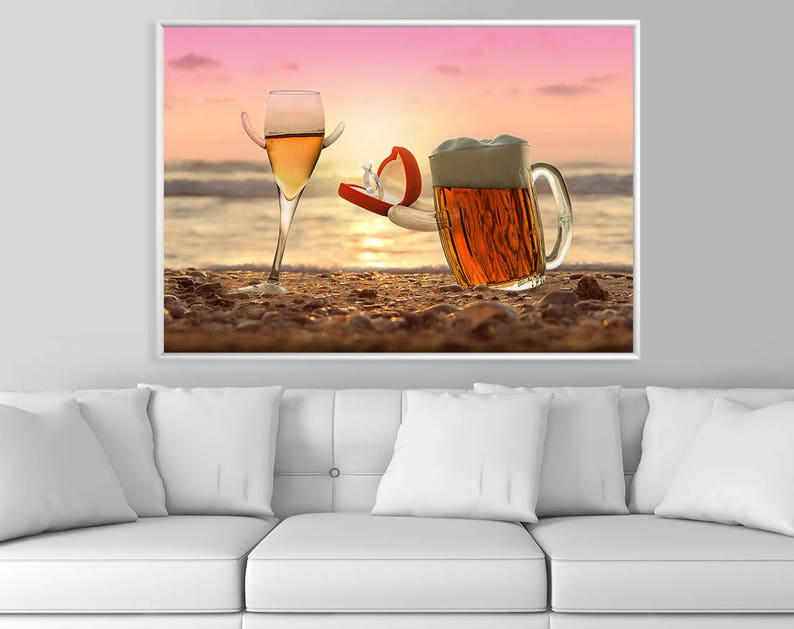 May include: A glass of white wine and a glass of beer on a sandy beach at sunset. The beer glass is holding a red ring box with a diamond ring inside.