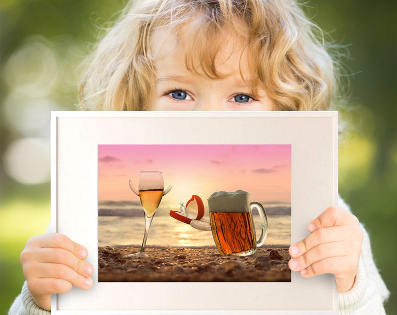 May include: A framed picture of a glass of wine and a beer mug on a beach at sunset. The wine glass has a ring on the rim and the beer mug has a ring on the handle. The ring is in a red box.