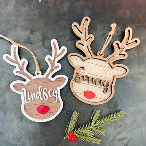 May include: Two wooden reindeer ornaments with white outlines. The reindeer have red noses and are personalized with the names "Lindsey" and "Sonny".