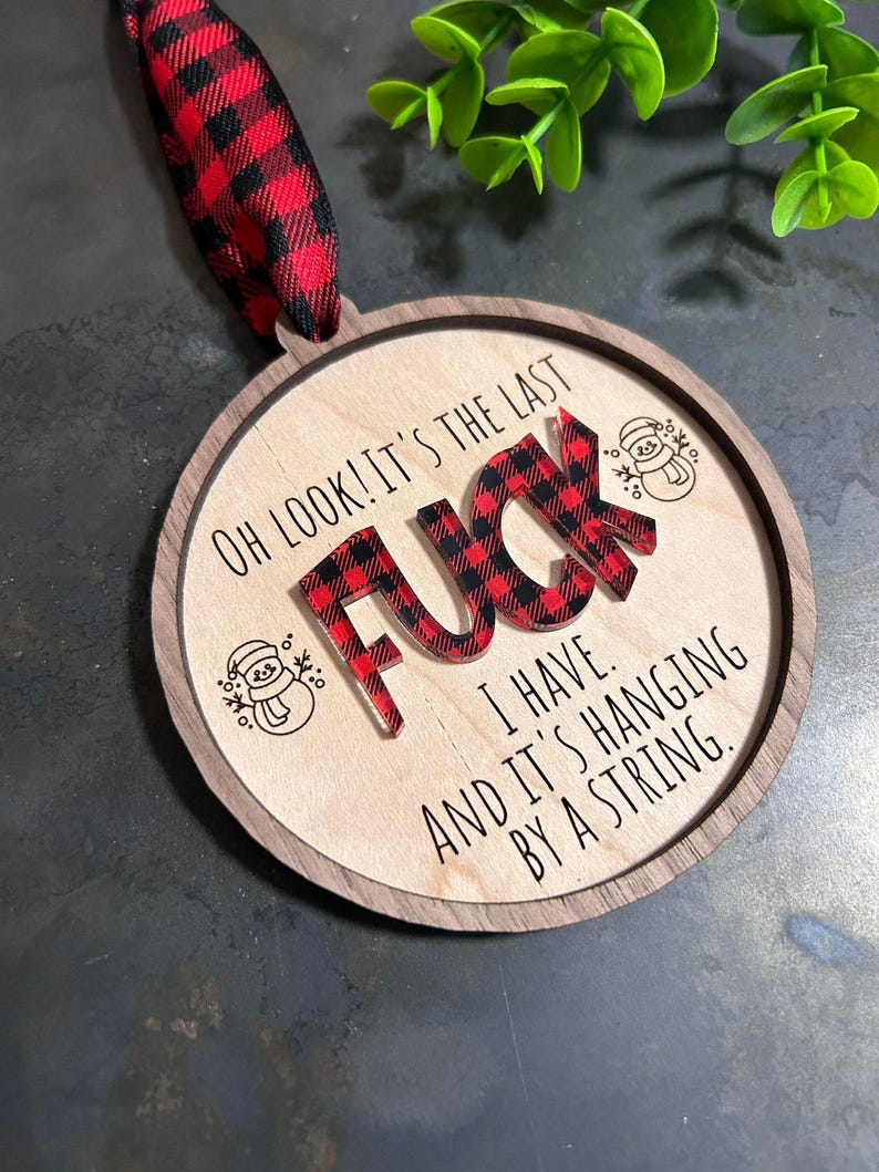May include: Round wooden ornament with a red and black plaid design. The ornament says "Oh look! It's the last F**k I have. And it's hanging by a string."