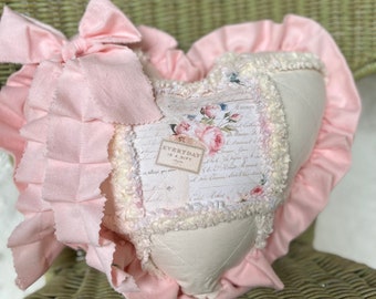 May include: A heart-shaped pillow with a white fabric base and pink ruffled trim. The pillow is decorated with a patchwork design featuring floral patterns and handwritten text, including the words "Everyday is a Gift".